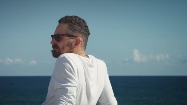 Güneşli bir günde denizin önünde oturan adam — Stok video