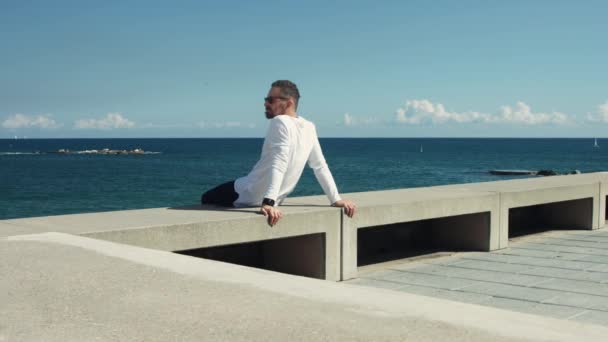 Homme assis devant la mer dans une journée ensoleillée — Video