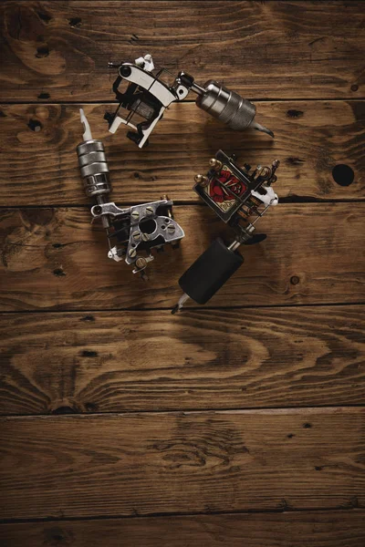 Three tattoo guns arranged on a brown wooden table — Stock Photo, Image