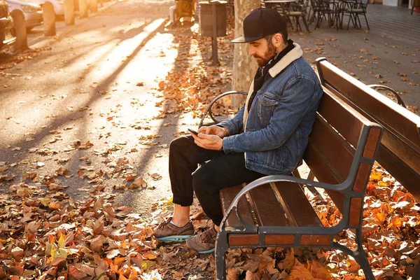 Hipster op een bankje met smartphone — Stockfoto