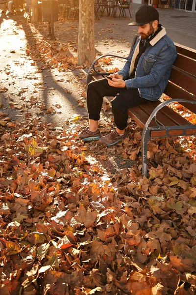 Hipster op een bankje met smartphone — Stockfoto