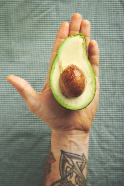 Männerarm mit halber Avocado — Stockfoto