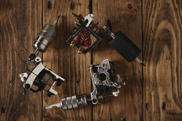 Three tattoo guns arranged on a brown wooden table — Stock Photo, Image