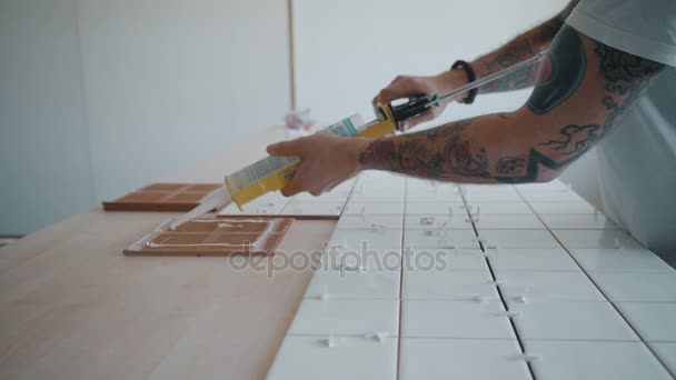 Homem tatuado aplica telhas cerâmicas no conjunto de mesa da cozinha — Vídeo de Stock