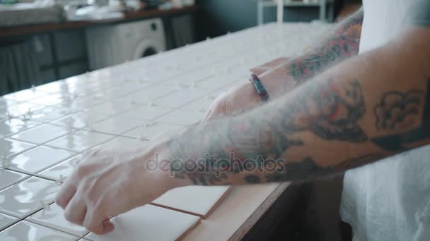 Татуированный человек наносит керамическую плитку на кухонный стол — стоковое видео