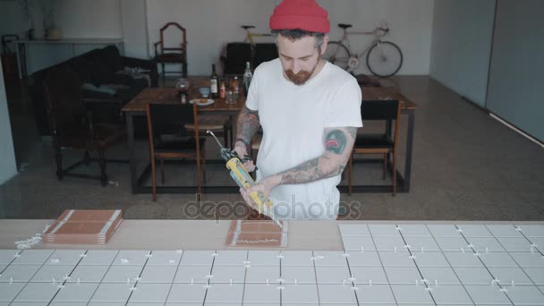 Homem tatuado aplica telhas cerâmicas no conjunto de mesa da cozinha — Vídeo de Stock