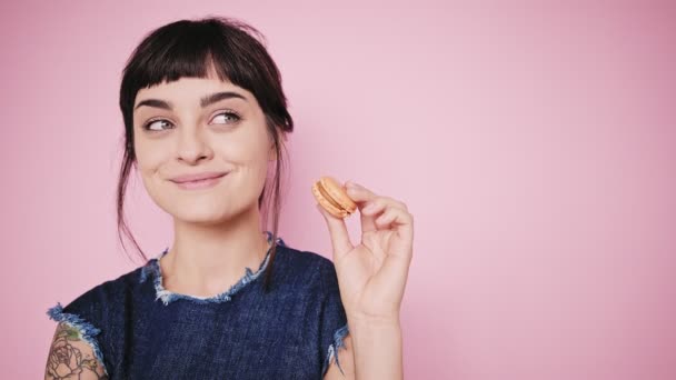 Aantrekkelijke brunette eet macarons geïsoleerd op een lichte achtergrond — Stockvideo