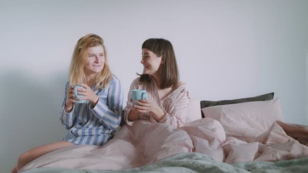 Две молодые женщины или пара, которые пьют кофе в постели — стоковое видео