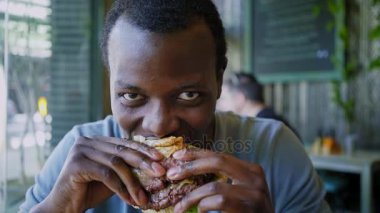 Mutlu siyah adam gülmek ve lezzetli et burger yiyen