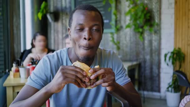 Feliz chico negro risa y come sabrosa hamburguesa de carne — Vídeos de Stock