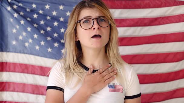 Blonde junge Frau singt vor amerikanischer Flagge — Stockvideo