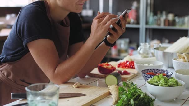 Jeune femme prépare le dîner dans la cuisine avec smartphone aide — Video