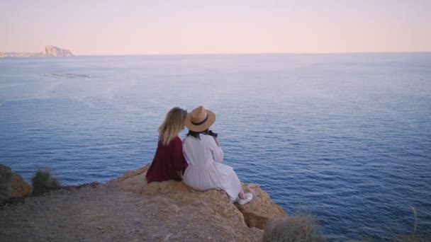 Two friends watch sunset while sitting on rocks — Stock Video