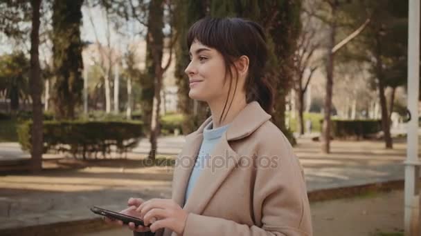 Молодая женщина гуляет в парке со смартфоном — стоковое видео