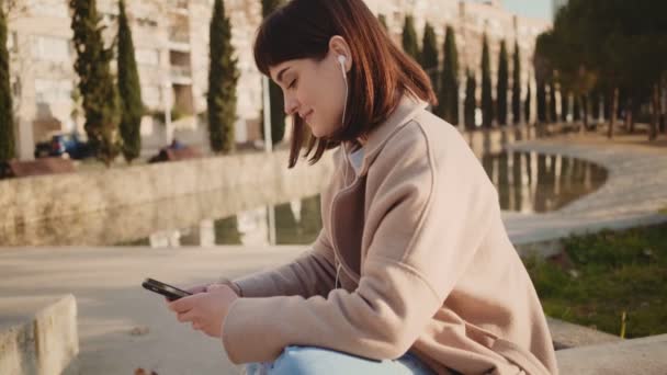 Flicka chattar med någon via telefon i park — Stockvideo