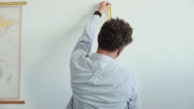 Adam ölçümleri cetvel ve kalem ile duvara yapar.