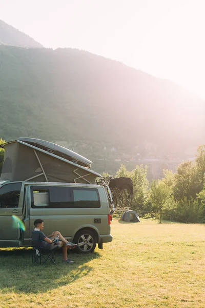 Viajante senta-se ao lado de van de acampamento ao pôr do sol — Fotografia de Stock