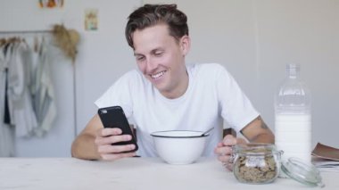 Yakışıklı genç adam Mısır gevreği ve telefon görünüyor