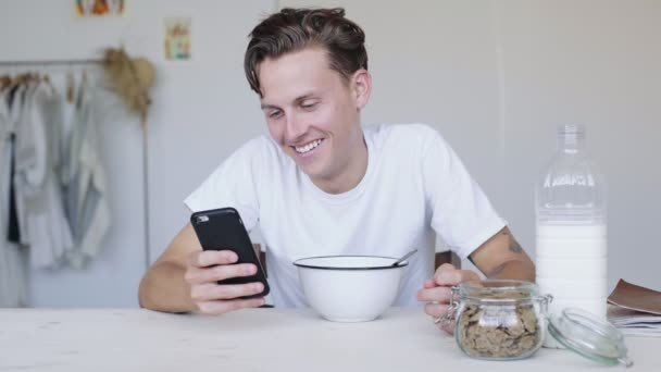 Bello giovane ha cereali per la colazione e guarda il telefono — Video Stock