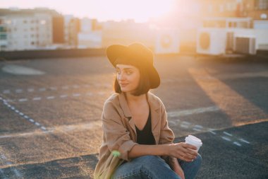 Genç model kahve fincanı günbatımı üzerinde tutar.