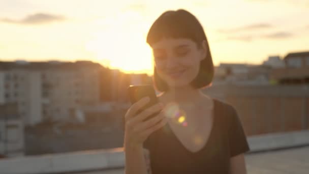 Bruna attraente con gadget sul tetto al tramonto — Video Stock