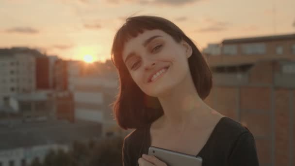 Ελκυστική μελαχρινή με gadget σε ταράτσα στο ηλιοβασίλεμα — Αρχείο Βίντεο