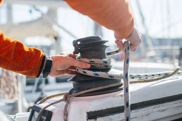 Professional sailor man ties up nautical rope on winch on boat