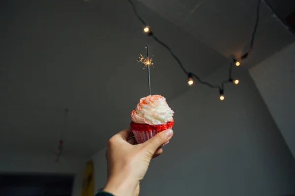 女性の手のフロスティングとピンクのカップケーキを押しウイップ クリームのトッピング ガーランドで部屋の壁に — ストック写真
