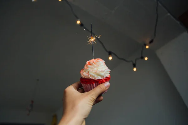 女性の手のフロスティングとピンクのカップケーキを押しウイップ クリームのトッピング ガーランドで部屋の壁に — ストック写真