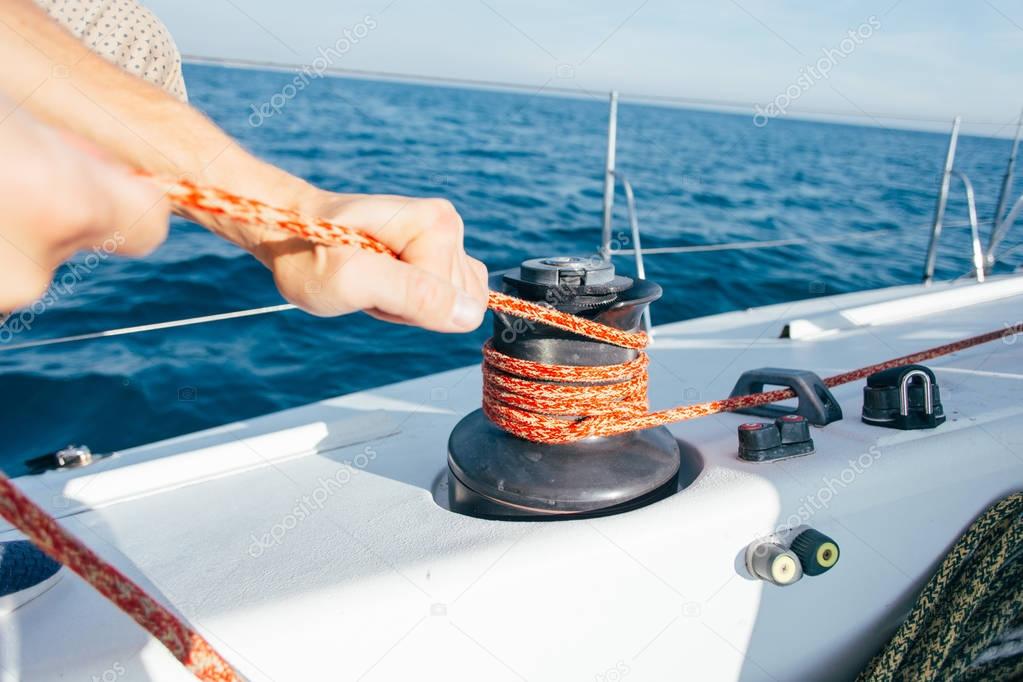 Professional sailor man ties up nautical rope on winch on boat