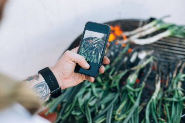 Adam Barbekü Izgara soğan ve gıda smartphone cep telefonu ile fotoğraf calcots ve yapar Pişirme