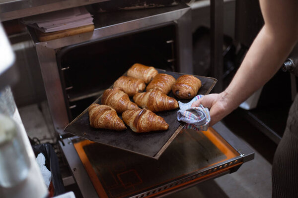 cropped view of baker holding tray with French croissants near opened oven