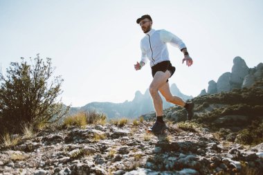 Güçlü ve sağlıklı orta yaşlı adam kayalar üzerinde çalışır ve kayalıklarla, ultra maraton veya rekabet, çalışan iz sırasında giyer profesyonel aktif giyim, güneş ışık parlama dağ Park, yaşam tarzı seçimleri
