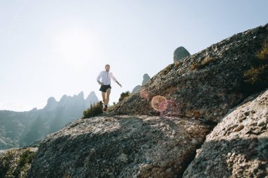 Adam şort ve ultra maraton iz ırk ya da sıcak güneşli, güzel manzarası ve manzara ile eğitim sırasında dağ yolu boyunca rock veya cliff Rüzgar ceket çalışır