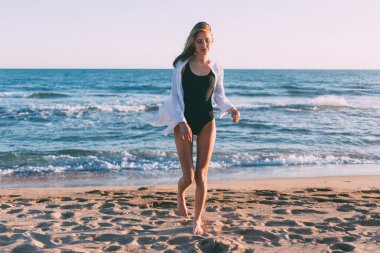 Güzel model boş sıcak güneşli plaj mavi su dalgaları ve yumuşak kum ile kamera için poz veriyor. Yaz aylarında rüyalar görünüm ilham verici şaşırtıcı seyahat hedef.