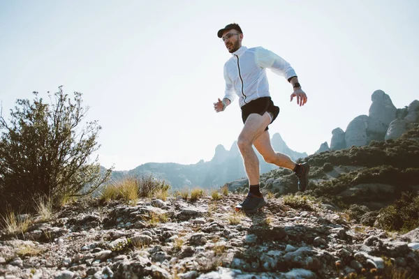 Strong and healthy middle aged man runs on rocks and cliffs, during ultra marathon or trail running competition, wears professional active wear, sun light flare in mountain park, lifestyle choices