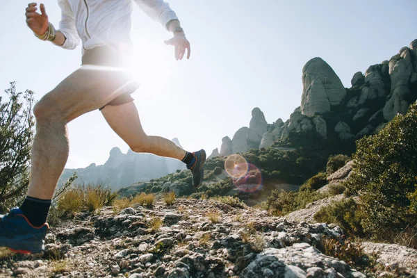 Strong and healthy middle aged man runs on rocks and cliffs, during ultra marathon or trail running competition, wears professional active wear, sun light flare in mountain park, lifestyle choices