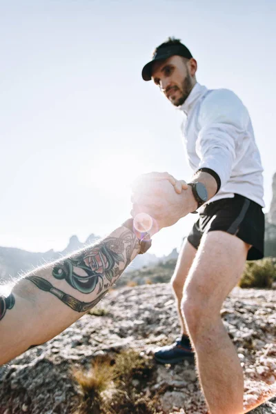 两个朋友或运动员帮助对方爬上陡峭的山坡或岩石在锻炼远足或训练 时髦运动爱好者与纹身 概念友谊和友谊 — 图库照片