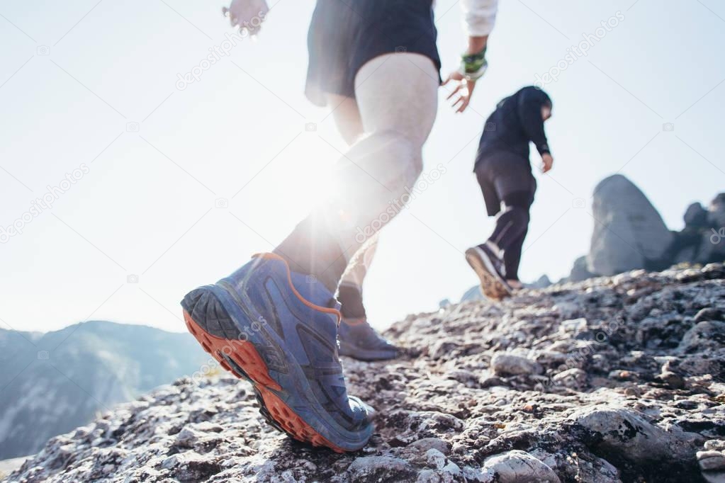 Two friends or athletes run on rocky mountain terrain on path or trail high in mountains or on coast, healthy lifestyle choice and hard workout plan. Sun flare into lens, inspiring movement