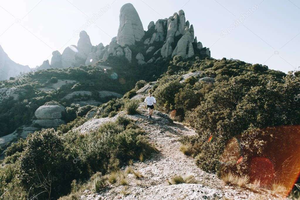 Figure or silhouette of athlete, sportsman or young runner run down a trail or path in mountains, among rocks and bushes. Enjoys fresh air and effort, sweat that turns into muscles and achievement