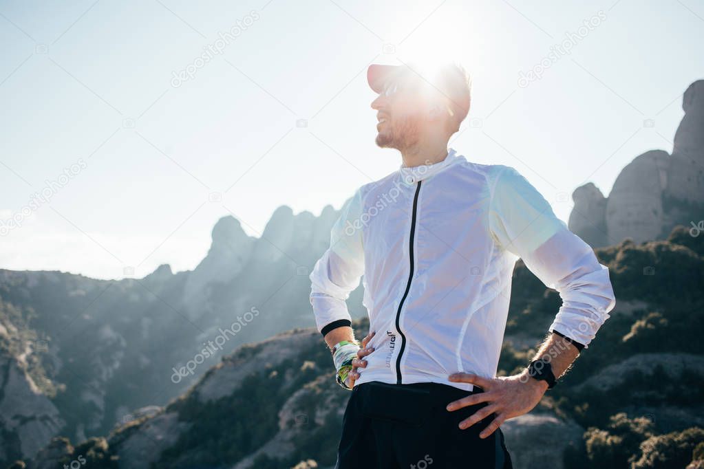 Portrait of handsome young man in running visor stands on top of mountain after extensive workout and strength training for ultra marathon trail running. Looks ahead confident and strong