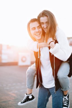 Aşık genç çift aptallar ve eğlenir çatısında gün batımında, gülmek ve gülümsemek, birbirimizi severek öpücük güzel güneş ışığı sızıntıları, domuz ride genç ilişki duygular, blogger yaşam tarzı ile