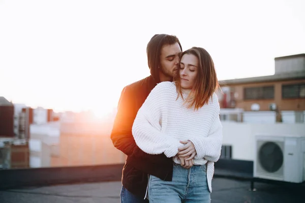 Beautiful and natural, real pretty couple of teenagers or millennials, cuddle and hug each other lovingly on top of rooftop in sunset. Inspiring relationship goals bloggers or lovers. new generation