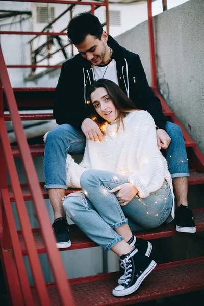 Beautiful and inspiring young couple cuddles, covered in decorative lights, sensual and warm tender photo of real feelings and relationship goals.