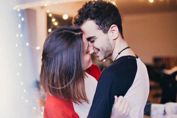 Cute and sensual young couple in love, smiling, hugging, cuddling and kissing inside house or apartment. Teenagers or millennials truly in love with each other, attractive boy and girl