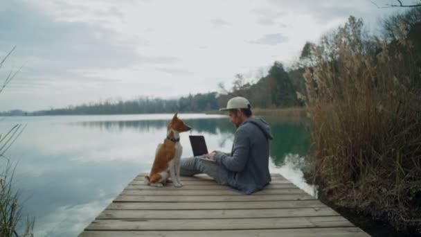 Freelancer works on his laptop outdoor next to lake, sitting on pond — Stock Footage Freelancer works on his laptop outdoor next to lake, sitting on pond Video Clip