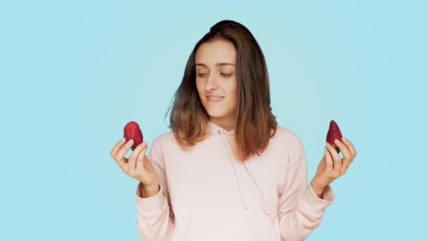 Junge Frau trifft die Wahl zwischen zwei Erdbeeren — Stockvideo