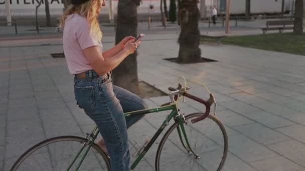 Menina bonita em sua bicicleta urbana vintage ao pôr do sol — Vídeo de Stock