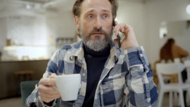 Orta yaşlı bir adam kafede telefonla konuşuyor.