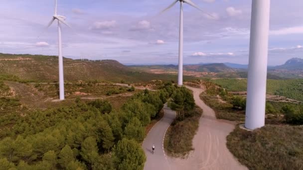 Велосипедист ездит между турбинной ветряной фермой на закате — стоковое видео